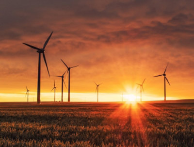 Turbine a vento in un campo che si stagliano su un tramonto intenso.