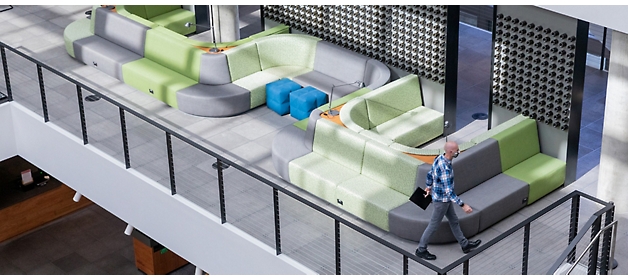 A man walks past modern, colorful seating arrangements in a spacious lobby with a balcony railing.