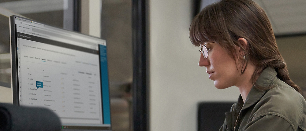 Kobieta w okularach koncentrująca się na ekranie komputera, na którym jest wyświetlany kod oprogramowania, w warunkach biurowych.