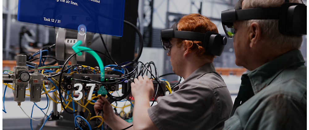 Two people using vr headsets work on a complex electronic device with wires and screens in a tech environment.