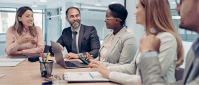 Diverse group of business professionals engaged in a meeting at a conference table with laptops and documents.