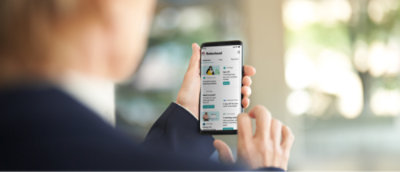 Person mit einem Smartphone, die eine App mit verschiedenen Blogbeiträgen auf dem Bildschirm durchsucht. Der Hintergrund ist unscharf.