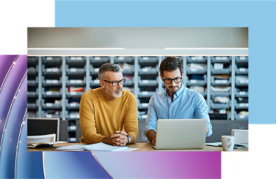 Two men, one in a yellow shirt and one in a blue shirt, looking at a laptop.