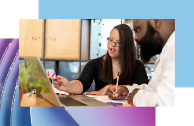 Dva profesionalca razgovaraju o radu preko laptopa i dokumenata u kancelarijskom okruženju.