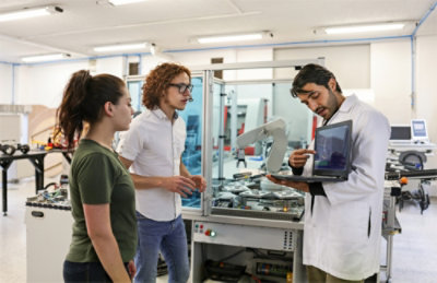 A group of people standing in a room with a man in a lab coat holding a laptop.