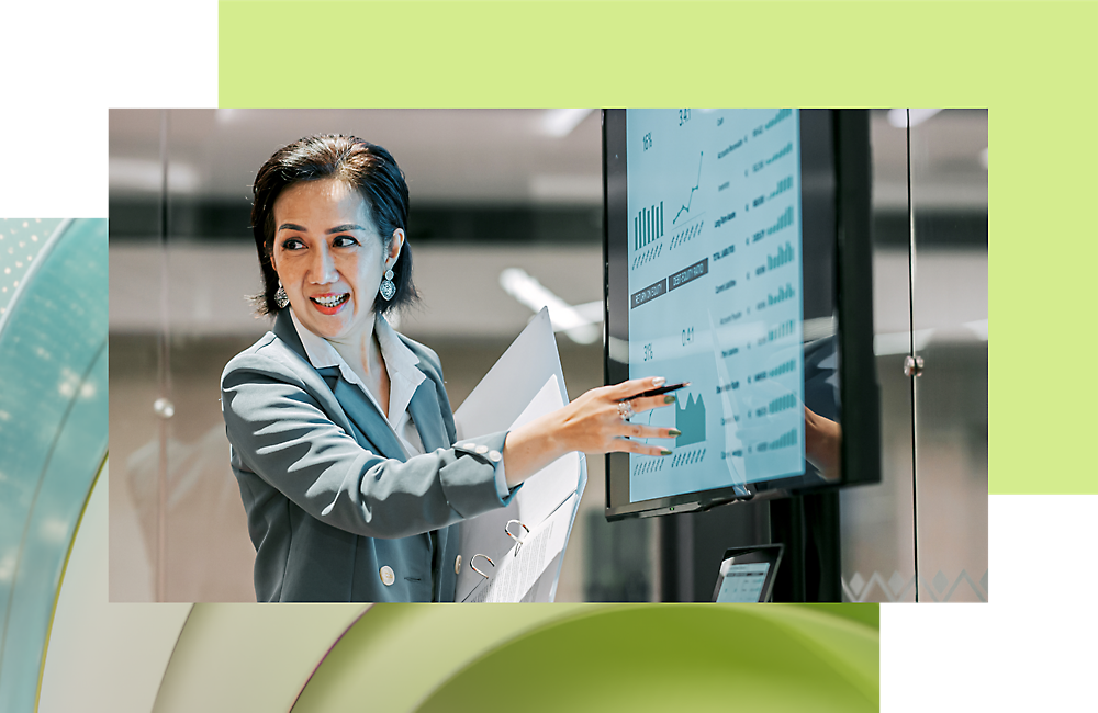 Uma mulher profissional a apresentar dados num ecrã digital, sorrindo e apontando, com um fundo de escritório moderno.