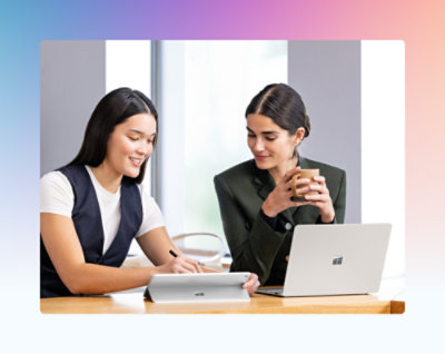 オフィスのテーブルに座り、ノート PC を見ている 2 人の女性。