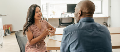 Mężczyzna siedzi przy blacie kuchennym, pracując na laptopie i trzymając kubek.