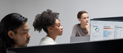 People seated at desks review analytics dashboards on computer monitors during a team meeting.