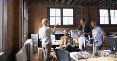 Kancelarija u kojoj četvoro kolega razgovaraju dok stoje i sede za stolom 