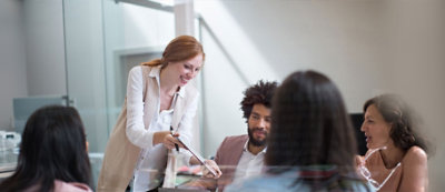Žena pruža dokument muškarcu sa laptop računarom u sobi za sastanke, dok još tri osobe