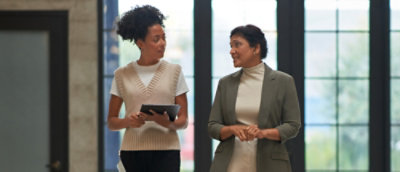 A woman in a suit holding a tablet while talking to another woman.