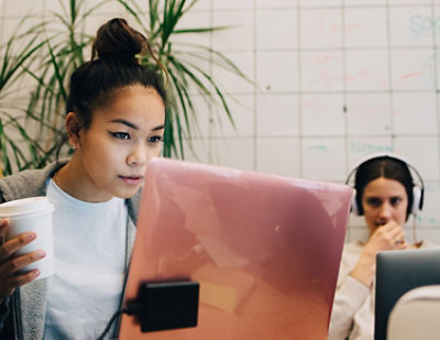 A woman with a bun holding a cup and looking at a laptop.