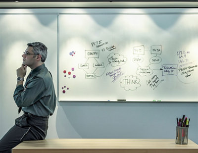 A man sitting at a table looking at a whiteboard with writing on it.