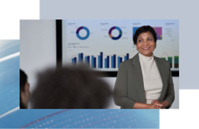 A confident woman in a blazer smiles while presenting in front of a screen showing pie charts and bar graphs.