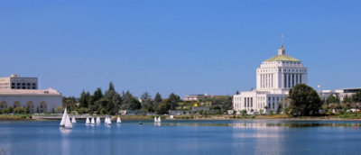  A landscape with blue sky, a lake with sail boats and government buildings in the background.