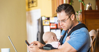 A person holding a baby and looking at his phone