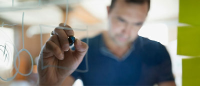 A person is drawing with a marker on a glass surface viewed from behind the glass.