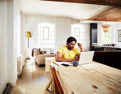 A man in a yellow shirt sitting at a table using a laptop.
