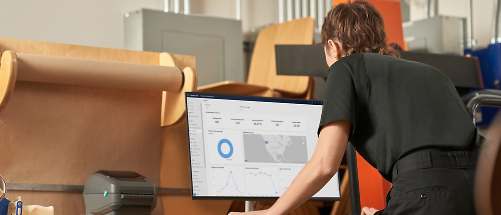 一个穿着黑色衬衫的人斜靠在桌子上，与显示图形和地图的大桌面屏幕上的数据交互
