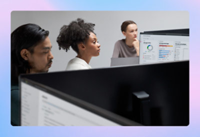 Three office workers focused on computer screens displaying graphs and data in a modern office setting.