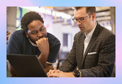 A man wearing glasses and a suit looking at a laptop.