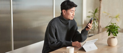  A person in a dark gray sweater uses a tablet and smartphone at a table with plants nearby.
