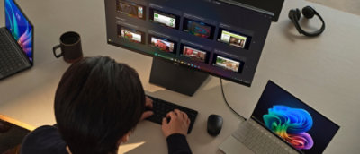 A person works at a desk with a large monitor, laptop, and coffee mug, multitasking in an office setting.