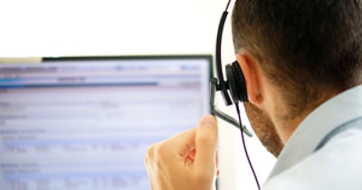 Una persona indossa le cuffie e guarda il monitor di un computer con uno schermo sfocato su cui è visualizzato del testo.