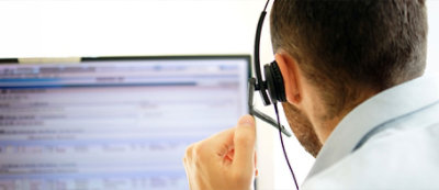 A person wearing a headset is looking at a computer monitor with a blurred screen displaying text.