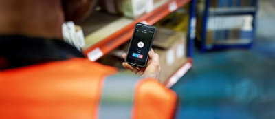 אדם מרכיב אוזניות ומחייך בזמן שהוא מחזיק תמונה ומביט במחשב נישא בסביבה מודרנית