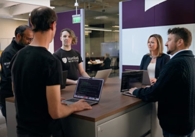 A group of people standing around a table with laptops.