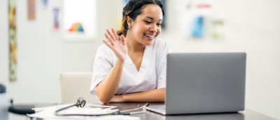 A doctor wearing a white coat, waving at a laptop screen.
