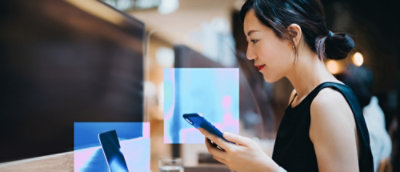 Person using smartphone beside computer screens