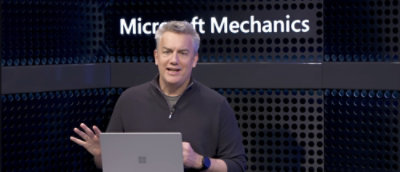 A person standing in fornt of a wall where microsoft mechanics is wirtten 