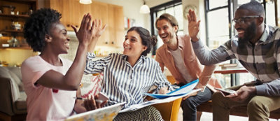A woman with curly hair is on a video call with five people, visible on her computer screen.