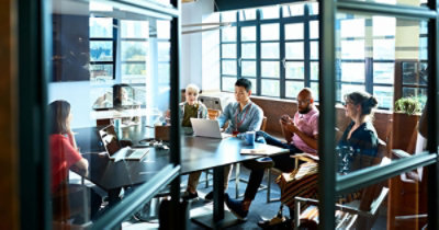 קבוצה מגוונת של אנשים יושבים סביב שולחן בחדר ישיבות במרחב משרדי מואר היטב, משתתפים בפגישה.