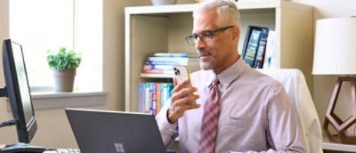 A man holding a phone and looking at a laptop.