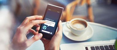 Osoba wchodzi w interakcję z chatbotem na ekranie smartfona. W tle znajduje się filiżanka kawy na talerzyku.