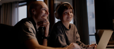 Two people sitting in an office space smiling at computer screens.