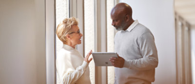 Two people standing up, in conversation. One person holding a Surface tablet device.