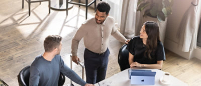 A group of men and a woman with long hair standing around a table in a room.