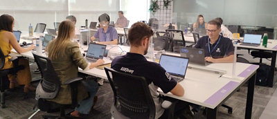 Grupo diversificado de funcionários da Gerdau colaborando em uma mesa compartilhada, cada um trabalhando em laptops em um escritório moderno e iluminado.