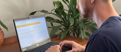 Um funcionário trabalhando de casa, focado em seu laptop. Ele está vestindo uma camiseta azul escura da Gerdau.