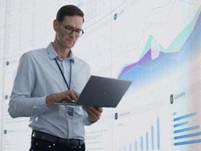 Osoba držící přenosný počítač před velkou obrazovkou.