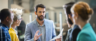 Several people standing together. One person talking to all, holding a piece of paper.
