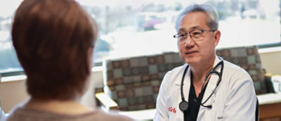 A hospital lobby, a male doctor in a Carle Health lab coat and stethoscope is talking to a woman with short, red hair.