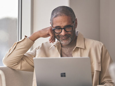 A man wearing glasses looking at the laptop and smiling