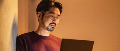 A man wearing glasses looking at the laptop and smiling