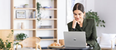 Person sitting at a round table in a modern office, working on a laptop with a coffee cup and pastry nearby.